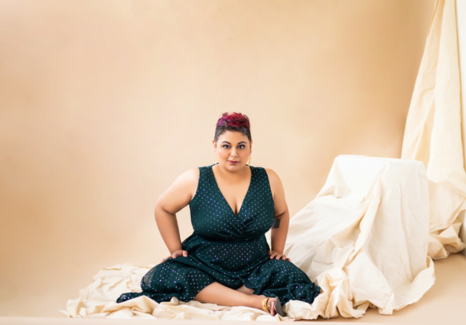 Farah seated on the floor in a teal polka-dot dress against a warm beige studio backdrop