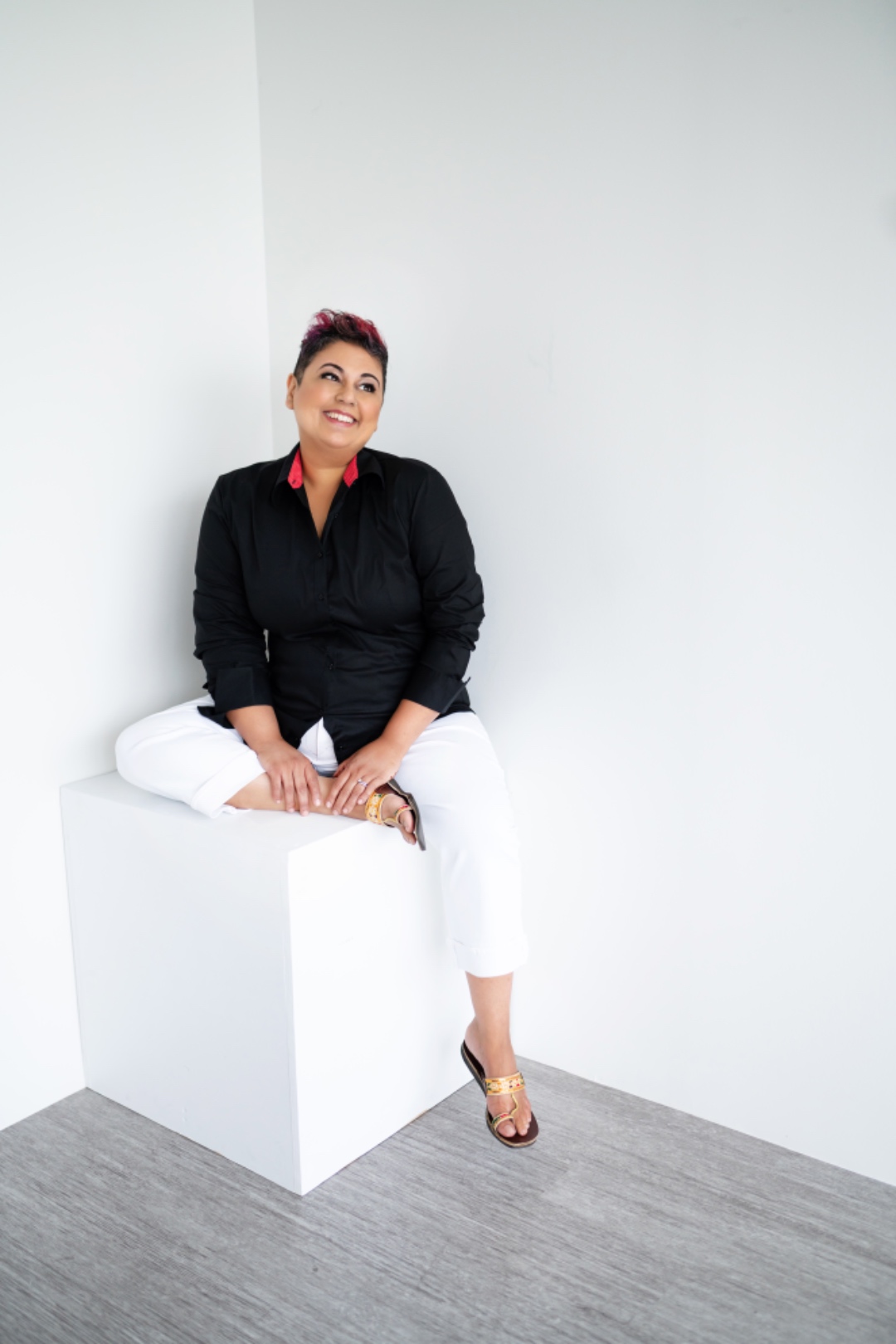 Farah seated on a white cube, looking upward and smiling