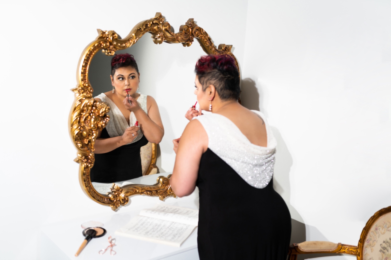 Farah in a performance gown applying lipstick at an ornate gold mirror