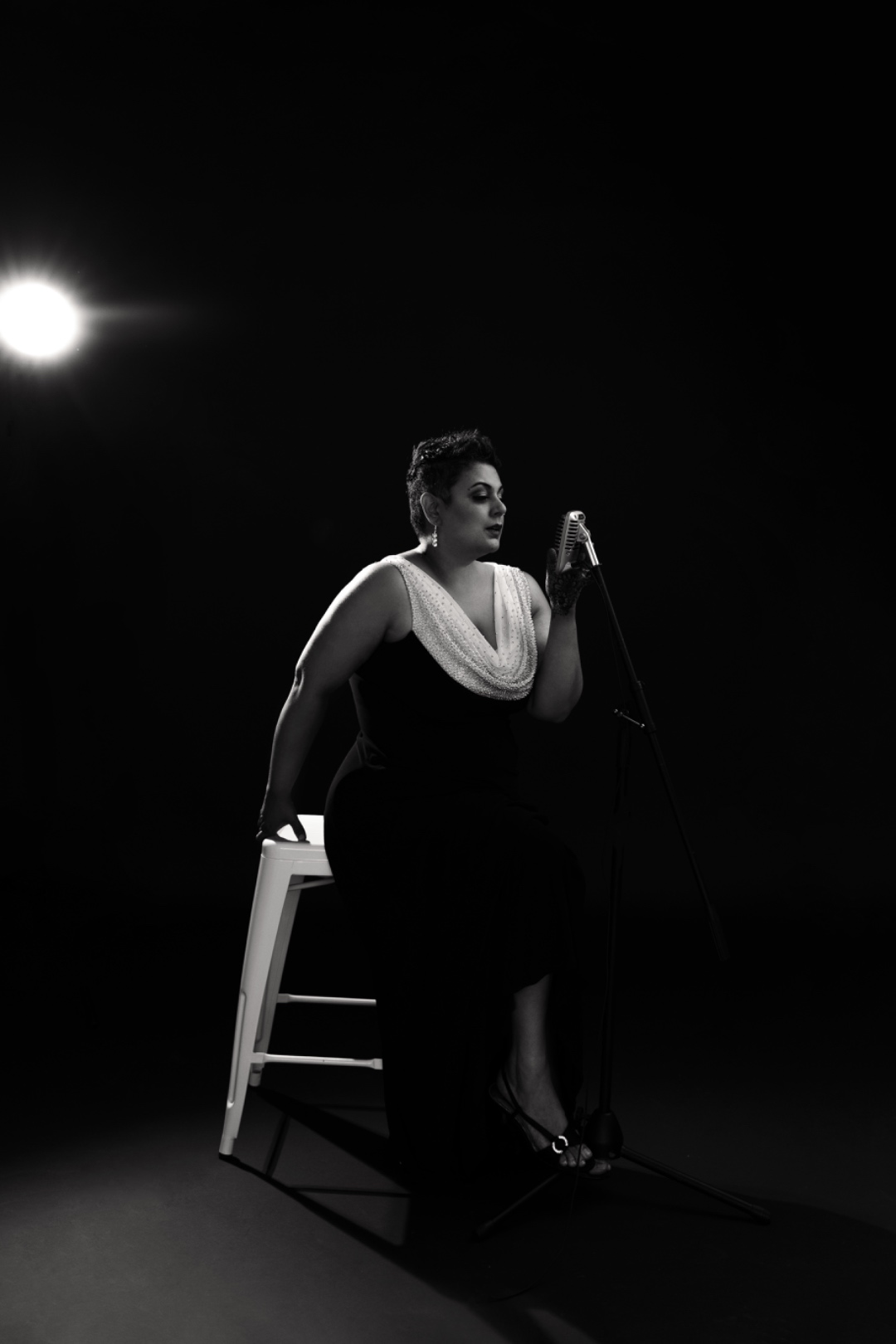 Farah performing on stage in black and white, leaning against a stool at the microphone